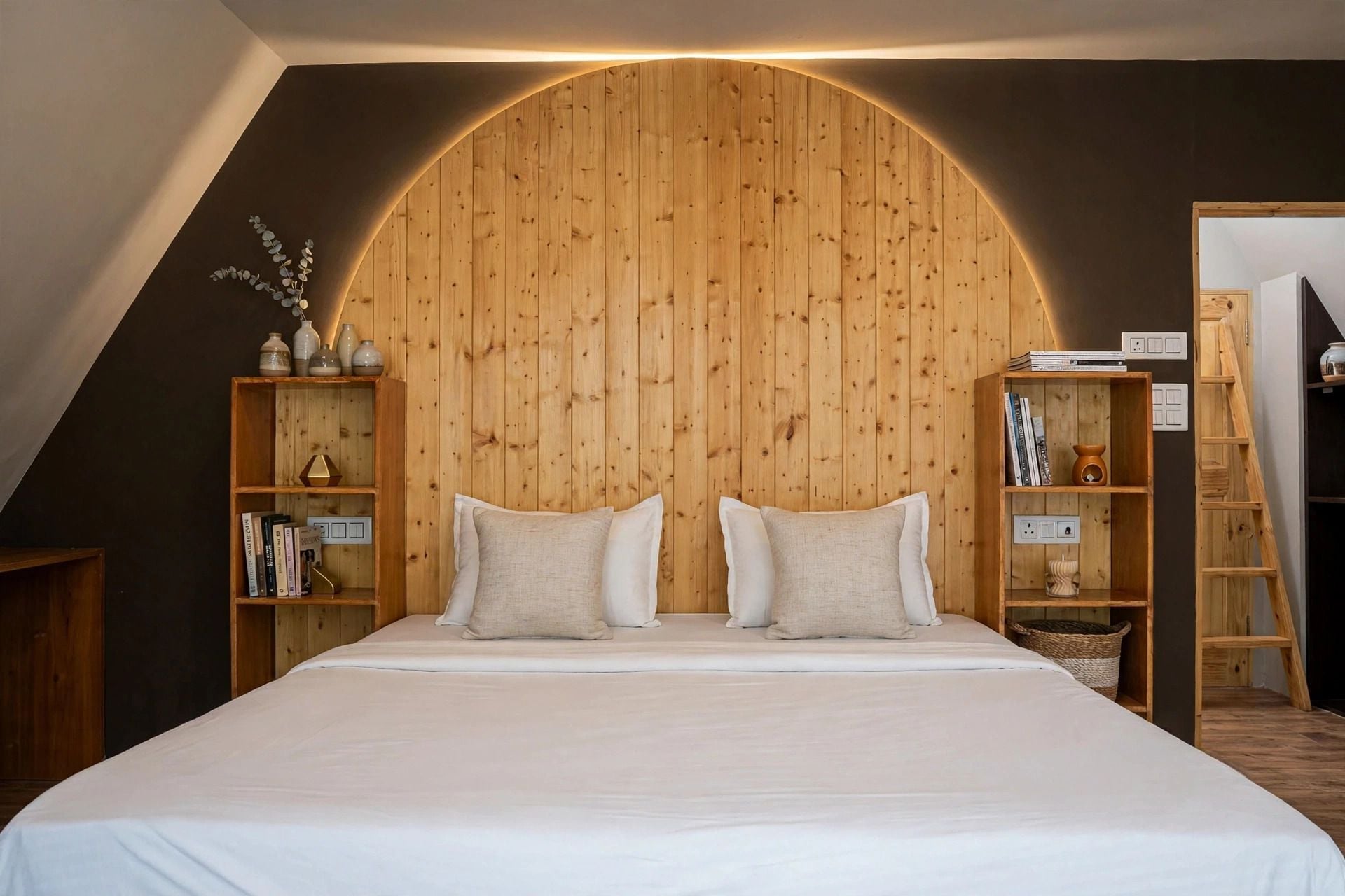 A bedroom with a sloped ceiling, a large bed with two pillows, wooden bookshelves, and a ladder.