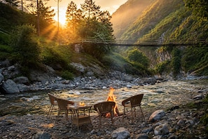 A riverside setting with a fire, chairs, and a table. - Raj Villas by Jomotel, Riverside Retreat (Banjar)