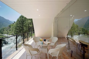 A balcony with wicker chairs and a table, overlooking a river and mountains. - Raj Villas by Jomotel, Riverside Retreat (Palach)