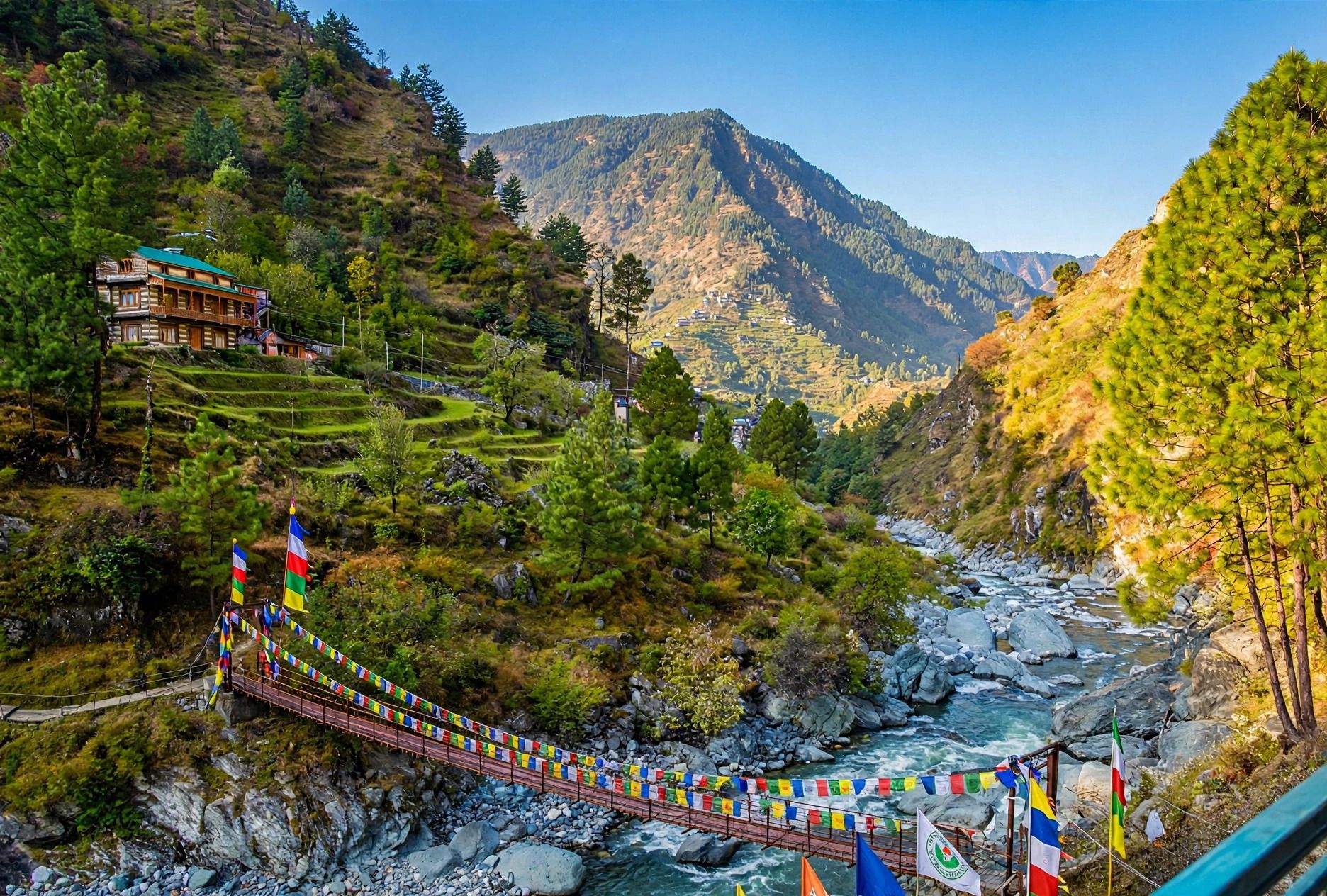 A suspension bridge with prayer flags, a mountain backdrop, and a building on a hillside.
