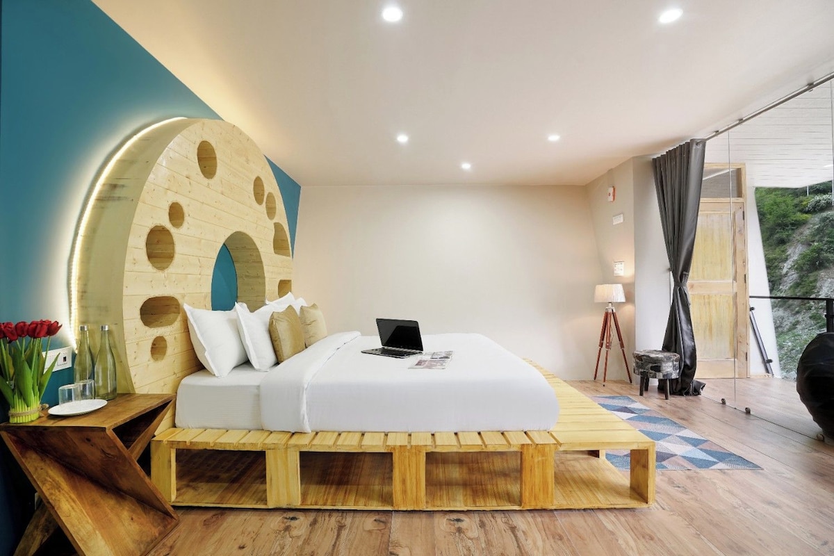 A modern bedroom with a wooden platform bed, a laptop on the bed, and a large circular wall feature.