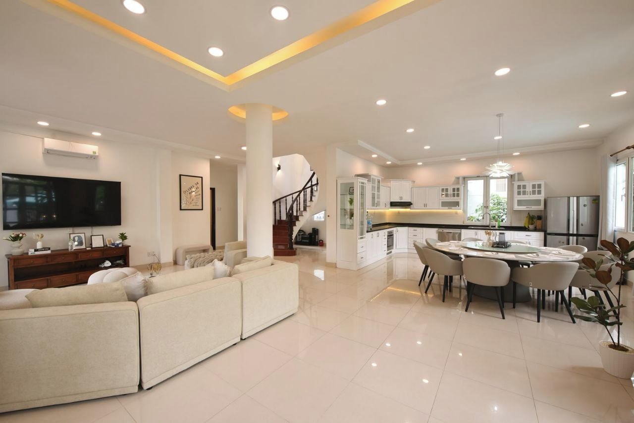 A modern living room with a large sofa, a dining area with a round table, and a kitchen with white cabinets.