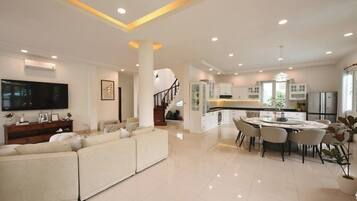 A modern living room with a large sofa, a dining area with a round table, and a kitchen with white cabinets.
