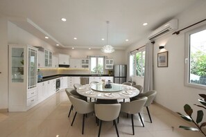 A modern kitchen with white cabinetry, a central island, and a dining area with a round table and chairs. - 6BR Pool Villa with Karaoke & Games Room, Thảo Điền, Sleeps 14 (Thành phố Hồ Chí Minh)