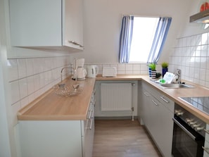 A modern kitchen with white cabinets, a wooden countertop, a built-in oven, and a window with blue curtains. - Flurstrasse - OG Right (Wyk auf Foehr)