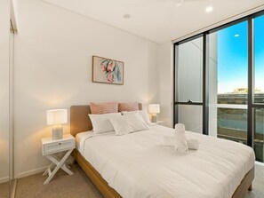 A modern bedroom with a large bed, two bedside tables, a nightstand, a window with a view, and a framed artwork on the wall. - 2BR West End Apt w/ Parking Walk to Convention Ctr (West End)