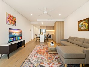 A modern living room with a flat-screen TV, sofa, coffee table, and a patterned rug. - 2BR West End Apt w/ Parking Walk to Convention Ctr (West End)