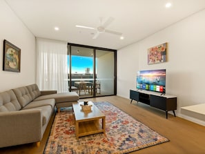 A modern living room with a sofa, coffee table, TV, and a view through a glass door. - 2BR West End Apt w/ Parking Walk to Convention Ctr (West End)