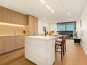 A modern kitchen with a central island, wooden cabinets, and a dining area with a view. - 2BR West End Apt w/ Parking Walk to Convention Ctr (West End)