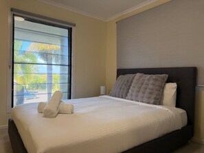 A hotel room with a large bed, a window with a view, and a bedside table with a lamp. - Ormiston Bayside Family Stay with Private Pool (Ormiston)
