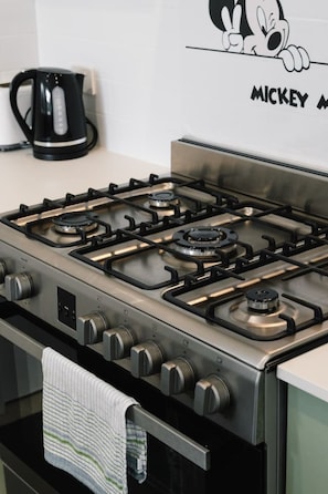 A kitchen with a stainless steel stove, a kettle, and a Mickey Mouse poster on the wall. - Spacious 4BR Family Home |Central Air-Con |Retreat (Pallara)