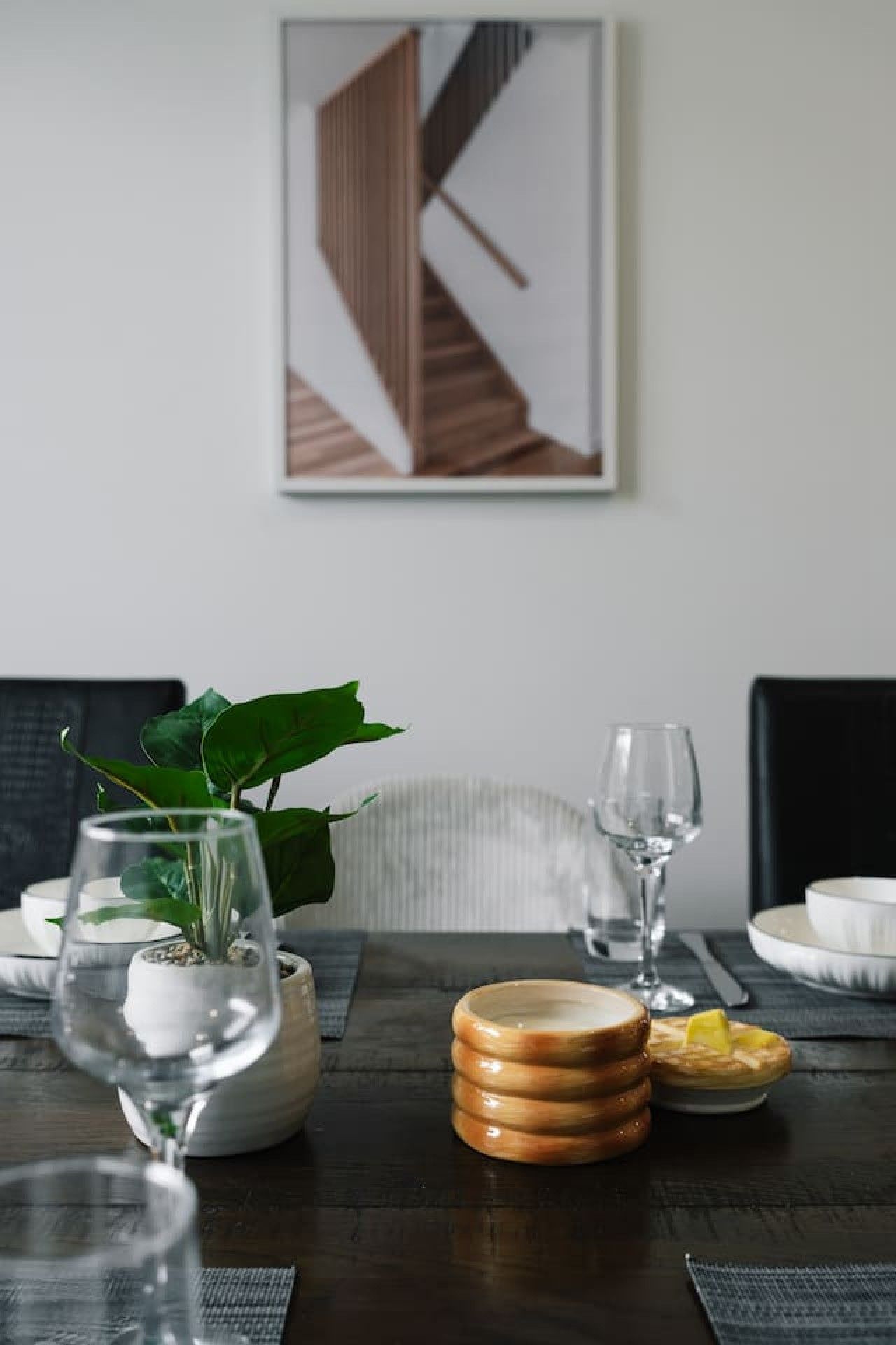 A dining table with a potted plant, wine glasses, and stacked plates.