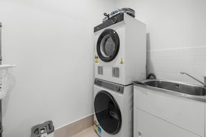 A compact laundry area with stacked washer and dryer, a sink, and a wall-mounted drying rack. - Spacious 4BR Family Home |Central Air-Con |Retreat (Pallara)