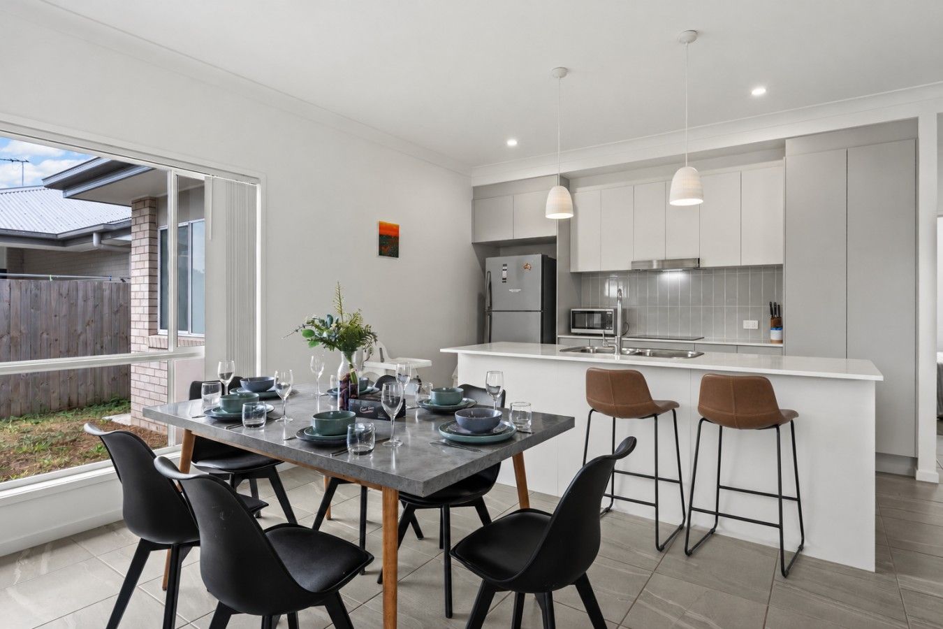 A modern kitchen with white cabinets, a central island with bar stools, and a dining area with a table set for four.