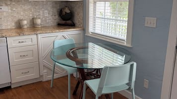 Una cocina con armarios blancos, una mesa de vidrio y una ventana con persianas.