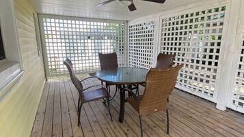 Un patio cubierto con una mesa y sillas, un ventilador de techo y un panel de celosía.