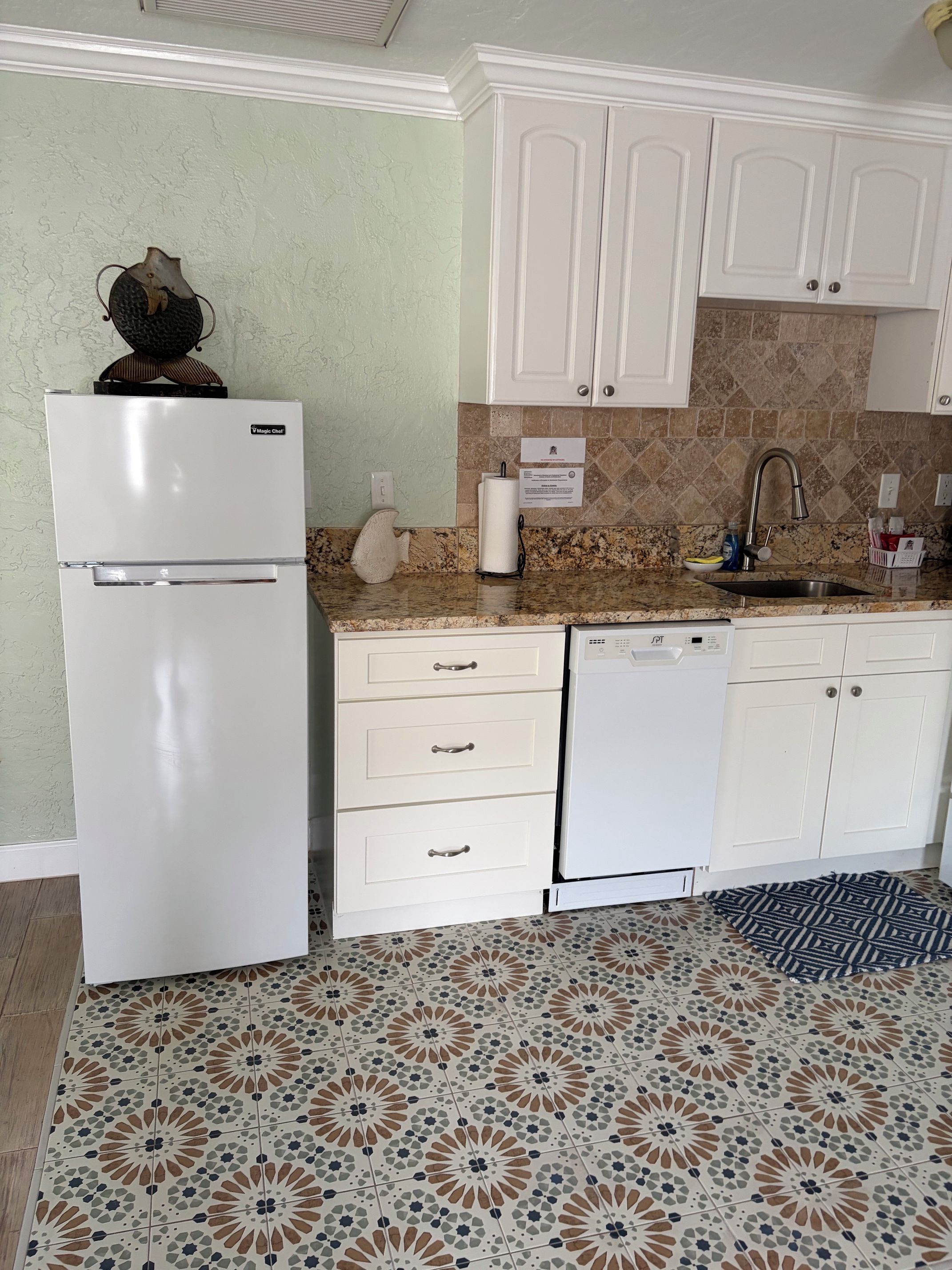 A kitchen with white cabinets, a white refrigerator, a dishwasher, and a patterned tile floor.