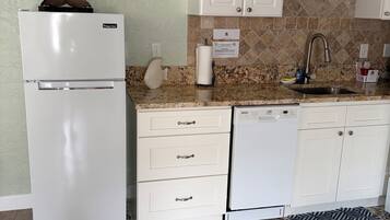 A kitchen with white cabinets, a white refrigerator, a dishwasher, and a patterned tile floor.