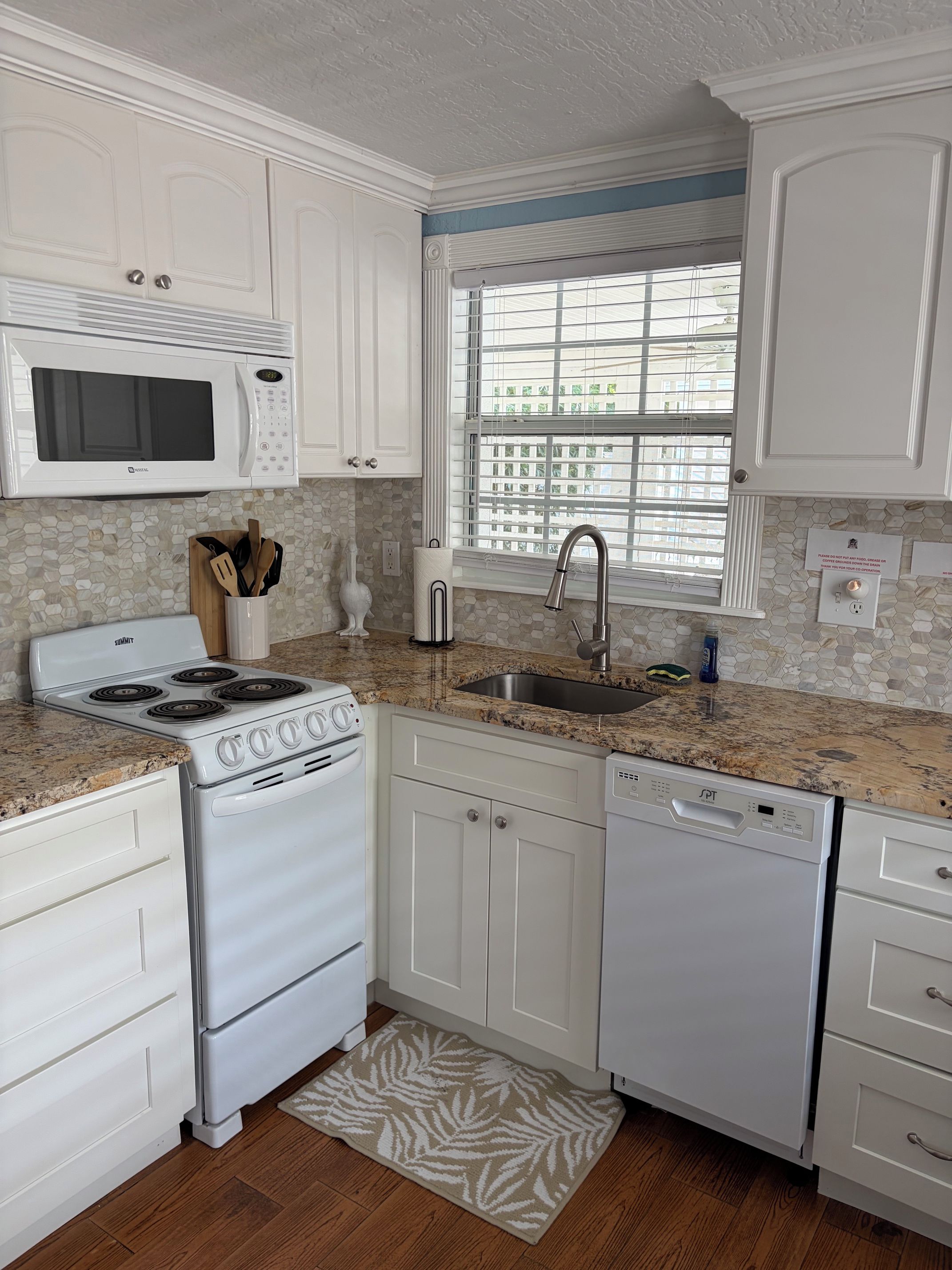 A kitchen with white cabinets, a microwave, stove, sink, and dishwasher.