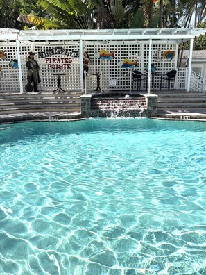 Une piscine aux eaux cristallines, agrémentée d’une cascade, entourée d’une clôture blanche ornée de poissons décoratifs et d’une statue de pirate.