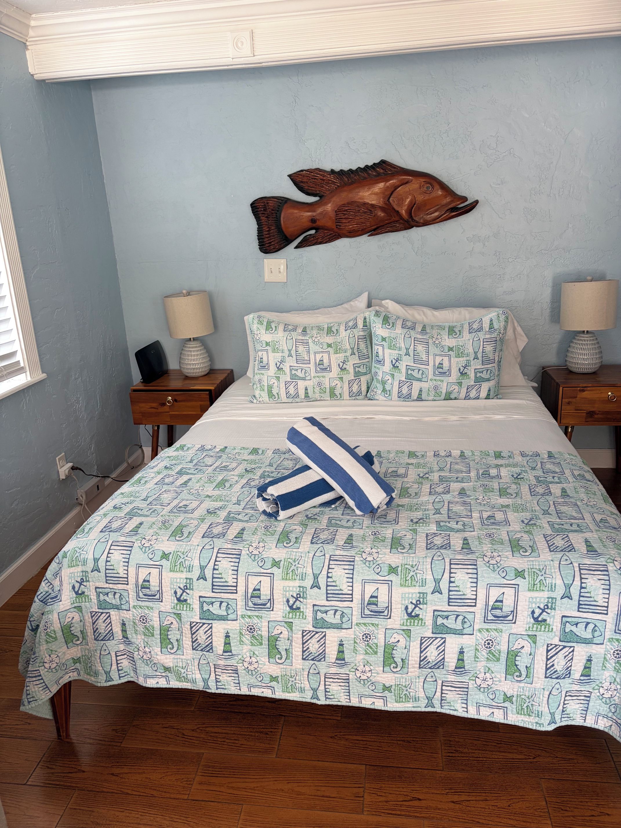 A bedroom with a bed, two nightstands, a wall-mounted fish decoration, and a patterned bedspread.