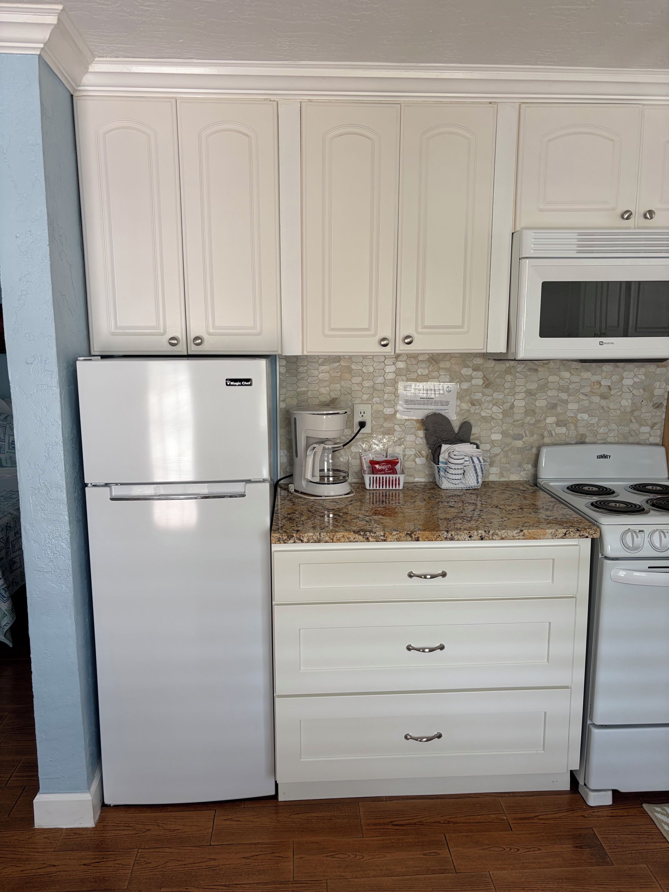 A kitchen with white cabinetry, a refrigerator, a coffee maker, a microwave, and a stove.