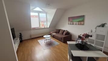 Eine moderne Lofts-Wohnung mit schrägem Dach, einem braunen Sofa, einem weißen Couchtisch, einem Gemälde und einer weißen Regaleinheit.