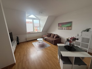 Un appartement moderne de style « loft » avec un plafond en pente, un canapé marron, une table basse blanche, un tableau et une étagère blanche.