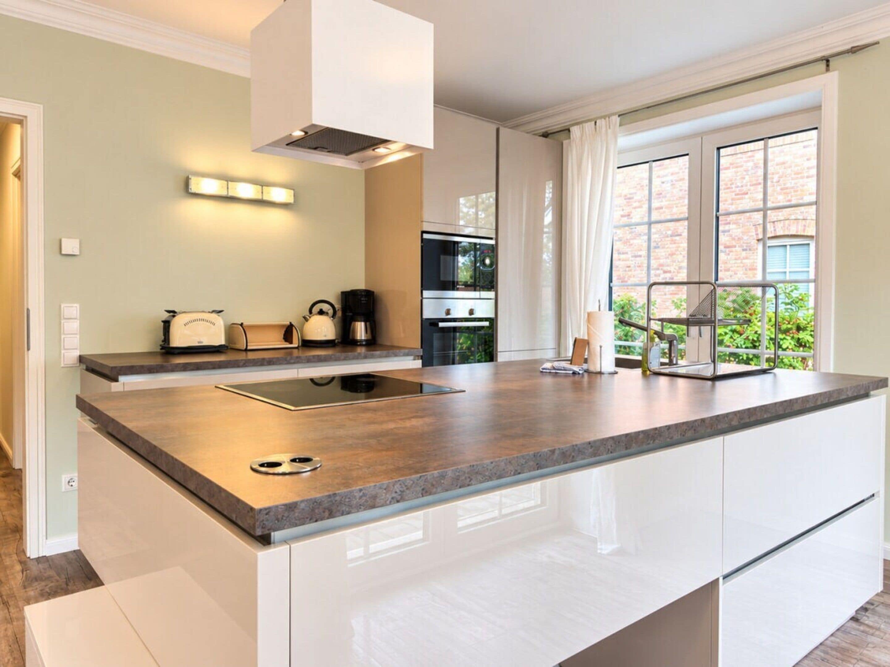 A modern kitchen with a central island, built-in appliances, and a large window offering a view of greenery.