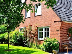 A red brick house with two windows, a garden with red flowers, and a bench. - EG - Jaardenhuug (Utersum)