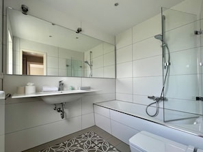 Ein modernes Badezimmer mit einer Duschkabine aus Glas, einem weißen Waschbecken mit Spiegel darüber und einem Musterboden.