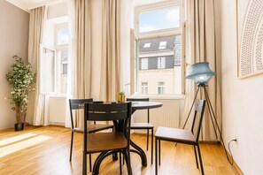 Ein Zimmer mit einem runden Tisch, Stühlen, einer Topfpflanze, einer Stehlampe und einem fenster mit Vorhängen.