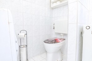 A bathroom with a toilet, a toilet paper holder, and a shower area. - Vienna Vibrant Center | Comfortable 2BR Apartment (Wien)