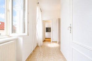 Ein Flur mit Heizkörper, einem fenster mit Vorhängen und einer Tür zu einer Küchenzeile.