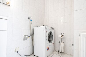 A compact, modern laundry room with a front-loading washing machine, a water heater, and a toilet paper holder. - Vienna Vibrant Center | Comfortable 2BR Apartment (Wien)