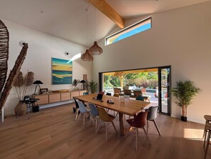 A modern dining area with a wooden table, chairs, and a view of an outdoor patio. - Oxéanide: Exceptional villa with a pool (Lacanau)