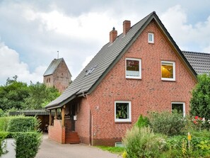Ein rotes Backsteinhaus mit geneigtem Dach, einer kleinen Veranda und einem Garten mit verschiedenen Pflanzen.