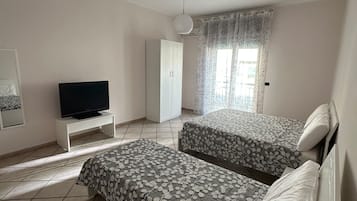 Ein Schlafzimmer mit einem Bett, einem Fernseher auf einem Schrank, einem Kleiderschrank und einem Fenster mit Vorhängen.