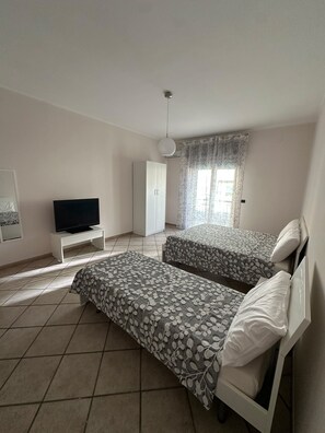 Ett sovrum med en säng, en tv på ett stativ, en garderob och ett fönster med gardiner.