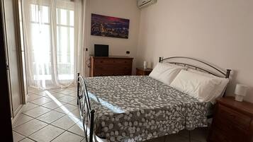 Une chambre à coucher comprenant un lit, une table de chevet, une commode, une fenêtre avec des rideaux et un appareil de climatisation.