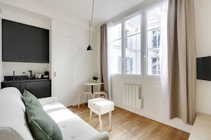 A modern, minimalist living space with a sofa, a small table, and a kitchen area. - Charmant Studio 2P - Palais Garnier (Paris)