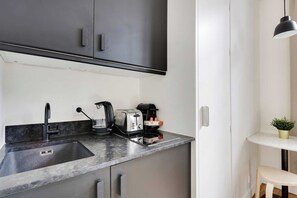 A modern kitchen with a built-in sink, a kettle, a toaster, and a coffee maker on the countertop. - Charmant Studio 2P - Palais Garnier (Paris)