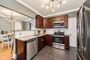 A modern kitchen with dark wood cabinets, stainless steel appliances, and a granite countertop. - Large Short North House - Hot tub, FirePit, Private Parking, Best Location (Columbus)
