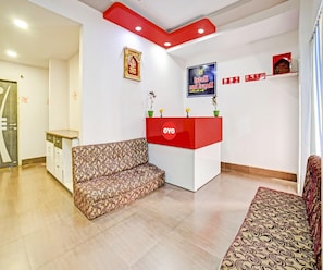 A reception area with a red counter, patterned sofas, a framed picture, and a poster on the wall. - Classic Nettoor (Adityapur)