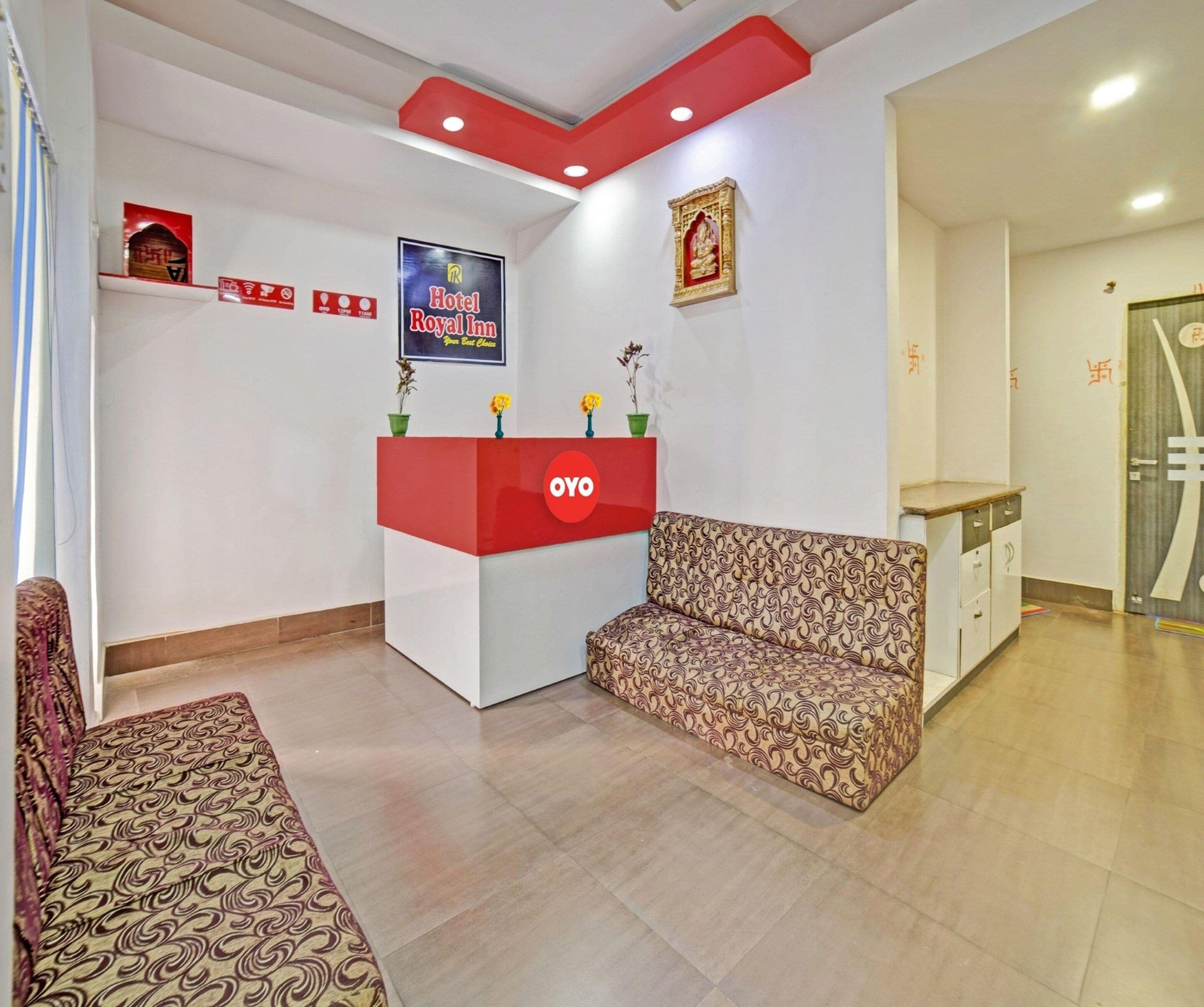Zona de recepción de hotel con un mostrador rojo y blanco, un sofá estampado y un cuadro en la pared.