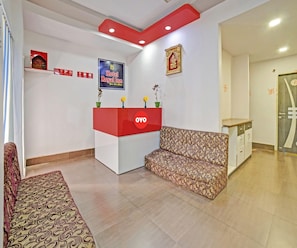 A hotel reception area with a red and white reception desk, a patterned sofa, and a framed picture on the wall.