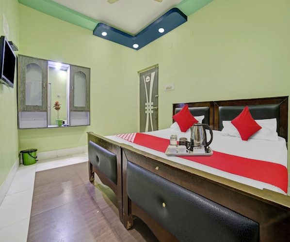 A hotel room with a bed, a bedside table with a kettle, a mirror, and a green bucket.
