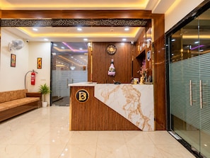 A reception desk with a wooden finish and a marble top, a fire extinguisher, a sofa, and a potted plant. - Hotel D3 And Rooftop Mansarovar Jaipur (Jaipur)