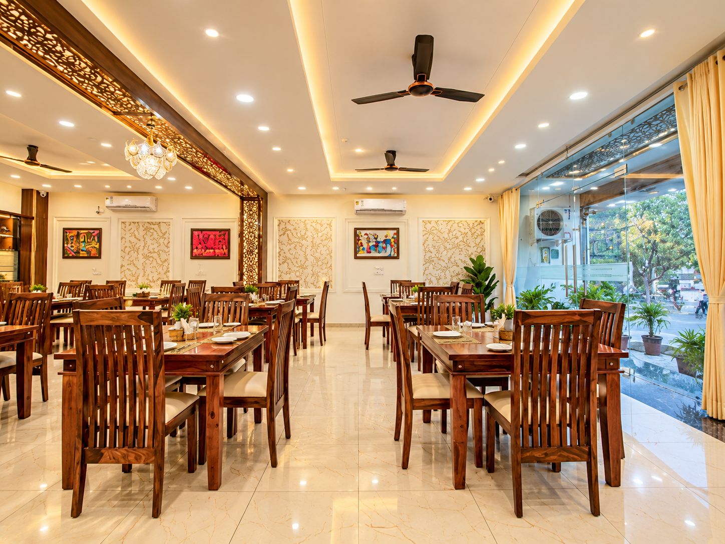 A spacious dining area with multiple wooden tables and chairs, ceiling fans, and decorative wall panels.