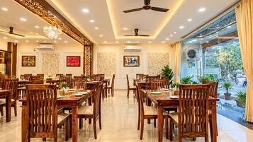 A spacious dining area with multiple wooden tables and chairs, ceiling fans, and decorative wall panels.